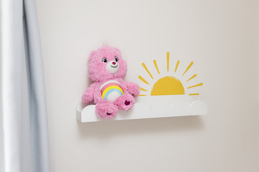 Pink teddy bear with a rainbow on a white shelf with a reusable yellow sun wall decal sticker against a light gray wall.