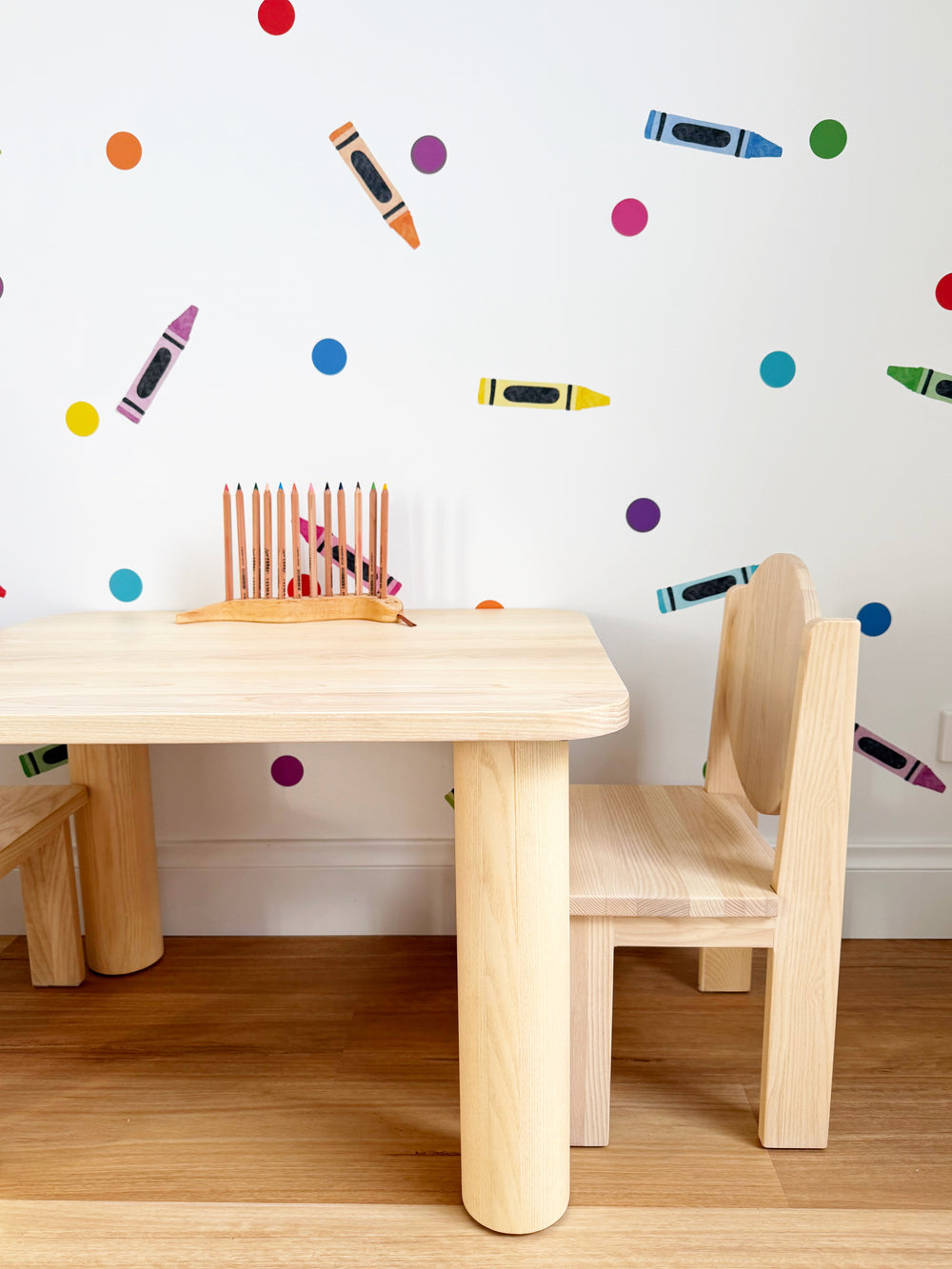 Colourful reusable wall paper stickers on a white wall, bright dots and bright crayons for kids playroom, nursery or bedroom. With child's wooden play table and chair 