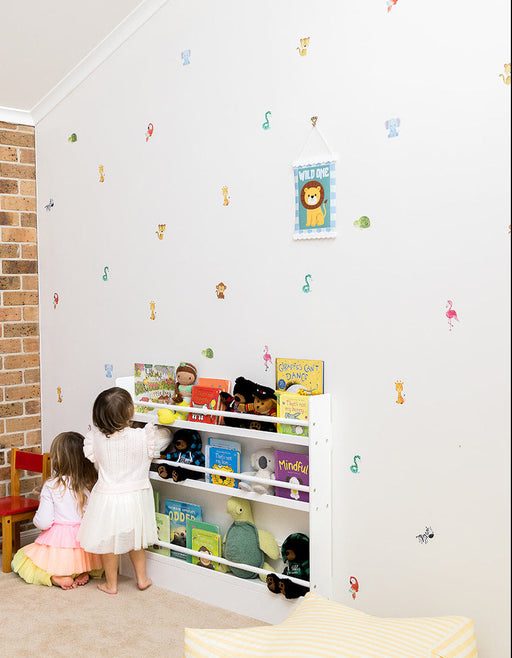 Children looking at books and toys on a shelf in a child-friendly room with jungle animal stickers on the wall.