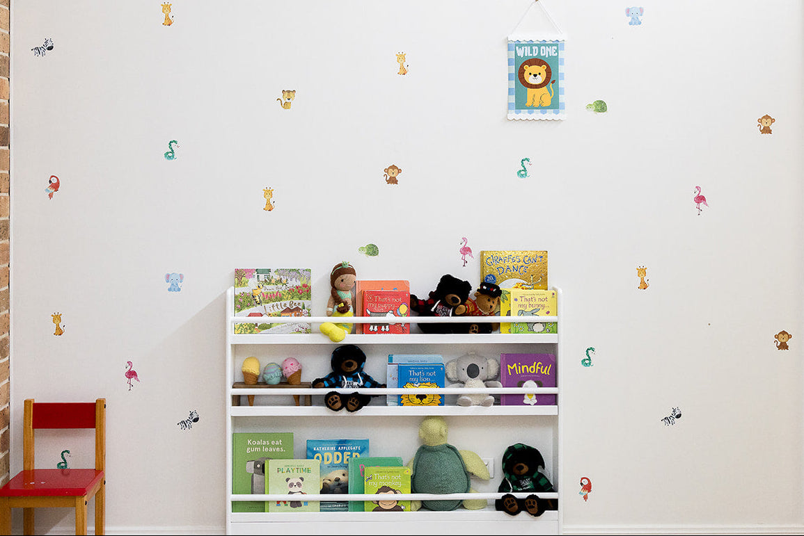 Children's bookshelf with books and toys against a white wall with decorative reusable jungle animal decal stickers.