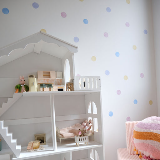 White dollhouse with toys inside, polka dot reusable wall decal stickers, and pink chair in a child's room.