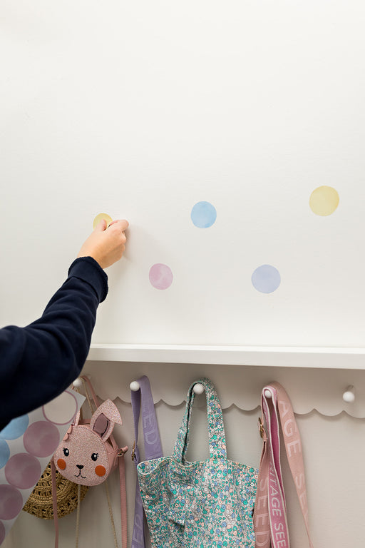 Child's hand reaching placing a reusable polka dot wall decal sticker on the wall with hanging bags below
