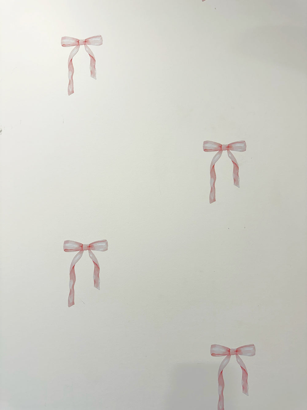 White wall with four small pink ribbon bow decals or stickers placed at different locations.