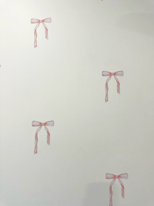 White wall with four small pink ribbon bow decals or stickers placed at different locations.